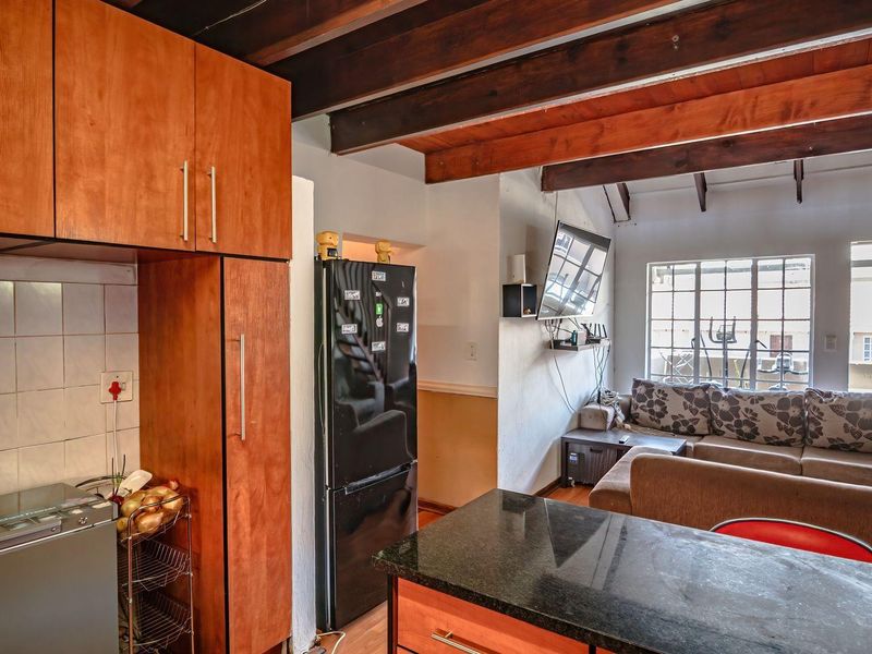 Open-plan living area featuring exposed timber ceiling beams, a kitchen with granite countertops, and direct access to a balcony through steel-framed windows.