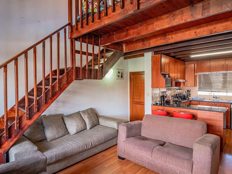 Open plan living area featuring a wooden staircase leading to a mezzanine level, integrated kitchen cabinetry, and laminate flooring throughout the space.