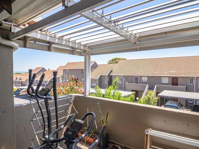A covered balcony featuring a louvred pergola and masonry balustrade, offering an elevated view of the surrounding residential complex.