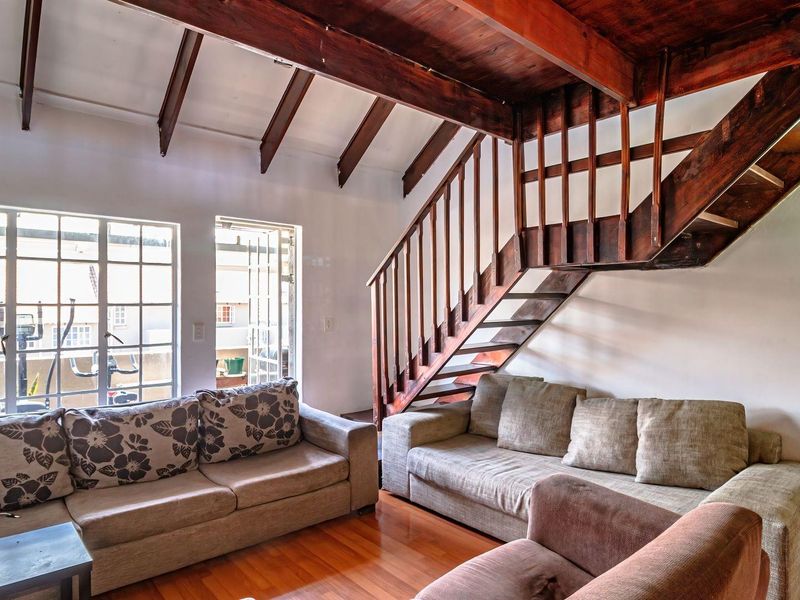 Spacious living area featuring exposed timber ceiling beams, a wooden staircase, and warm timber flooring, offering a rustic aesthetic with abundant natural light.