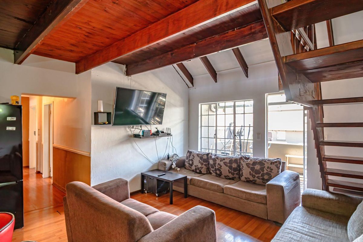 Living room featuring exposed timber ceiling beams, hardwood flooring, and a wooden staircase leading to an upper level with access to a balcony.