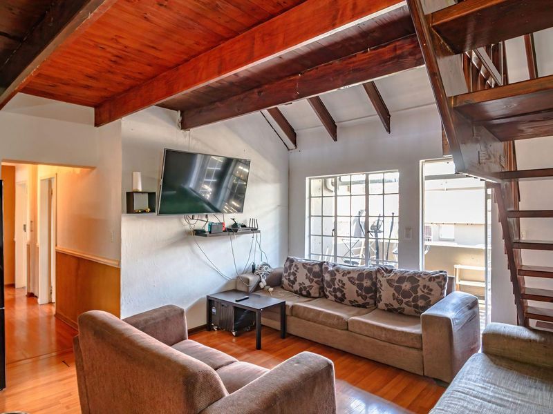 Living room featuring exposed timber ceiling beams, hardwood flooring, and a wooden staircase leading to an upper level with access to a balcony.