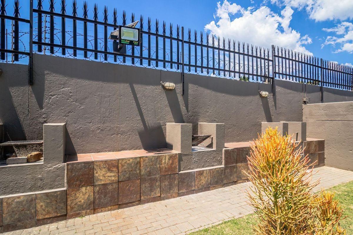 Outdoor entertainment area featuring built-in braai stations, paved walkway, and a secure perimeter wall with integrated lighting and security fencing.
