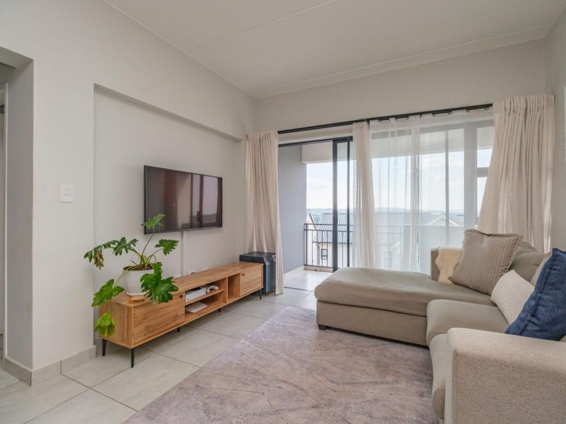 A bright living room featuring tiled flooring and a large sliding glass door providing access to a private balcony.