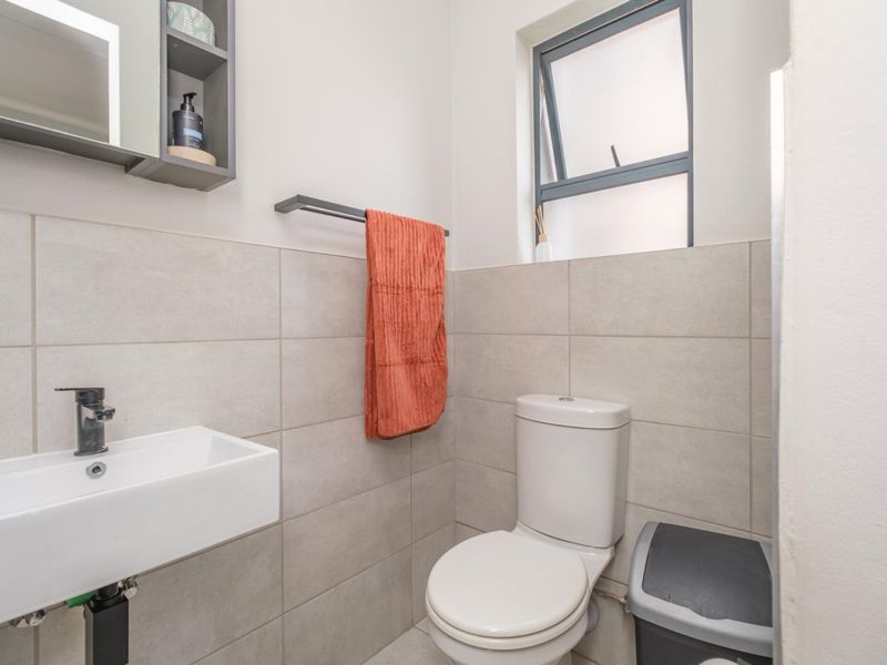 A modern, compact bathroom featuring neutral wall tiles, a wall-mounted basin, a toilet, and a functional top-hung window for ventilation.