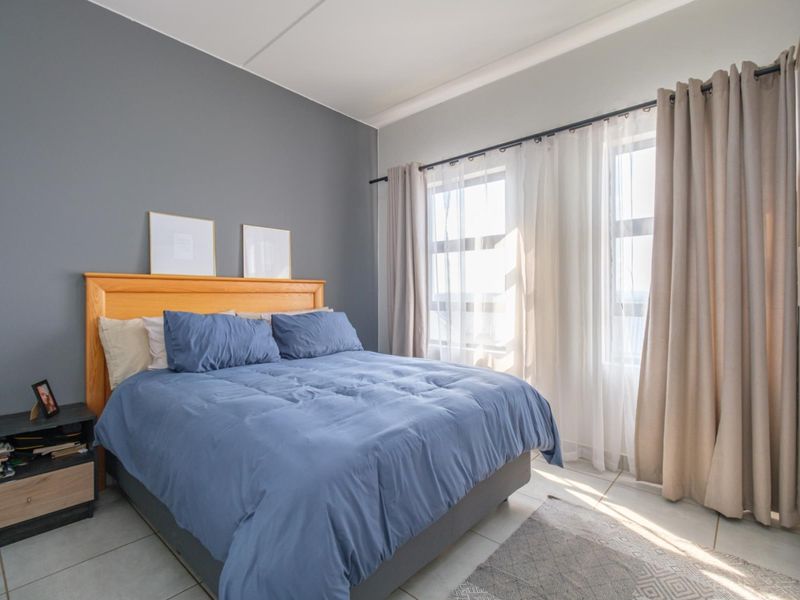 A well-lit bedroom featuring neutral tiled flooring, a grey accent wall, and a built-in cupboard with natural light from the window.