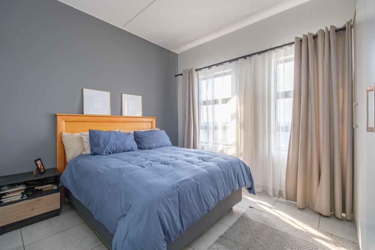 A well-lit bedroom featuring neutral tiled flooring, a grey accent wall, and a built-in cupboard with natural light from the window.