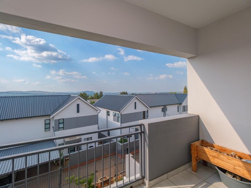 A covered balcony featuring tiled flooring and a metal balustrade, offering an elevated view of the surrounding residential complex.