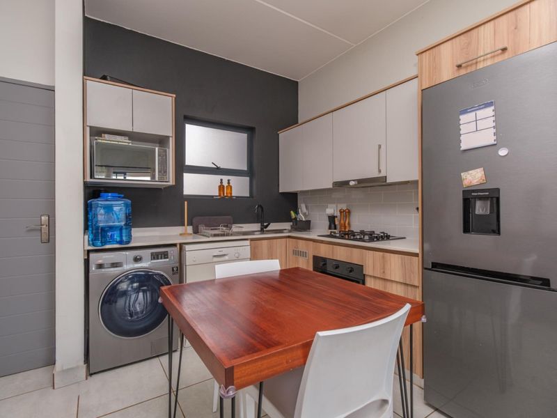 A modern, compact kitchen featuring light wood and grey cabinetry, a gas hob, built-in oven, and integrated laundry space with tiled flooring.