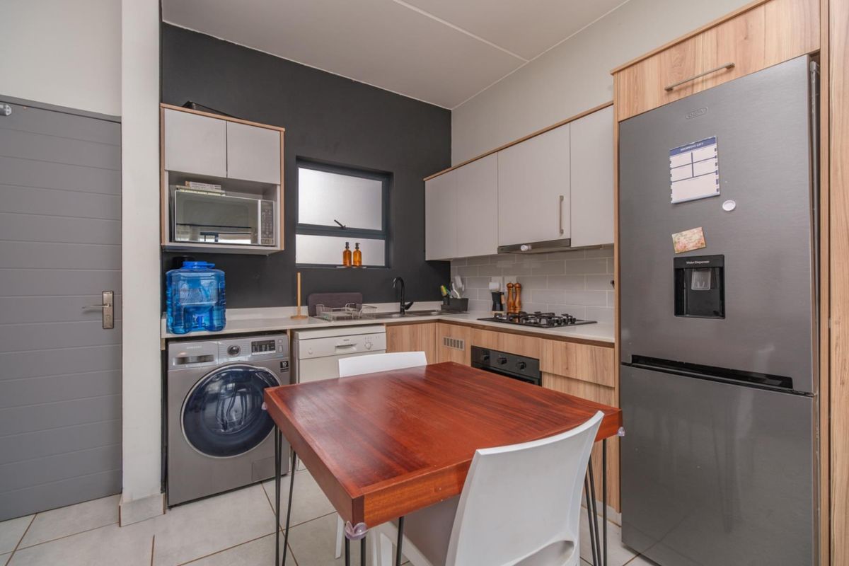 A modern, compact kitchen featuring light wood and grey cabinetry, a gas hob, built-in oven, and integrated laundry space with tiled flooring.