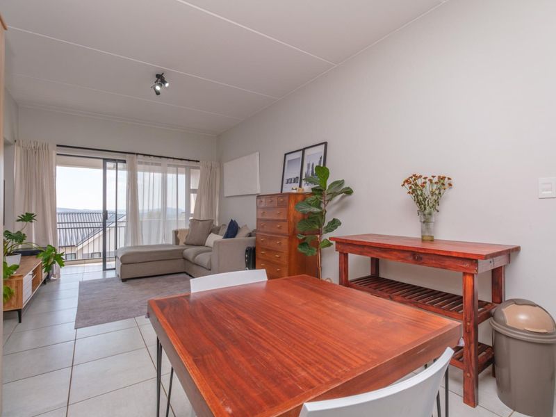 Open plan living and dining area featuring tiled flooring and large sliding glass doors leading to a balcony with scenic views.