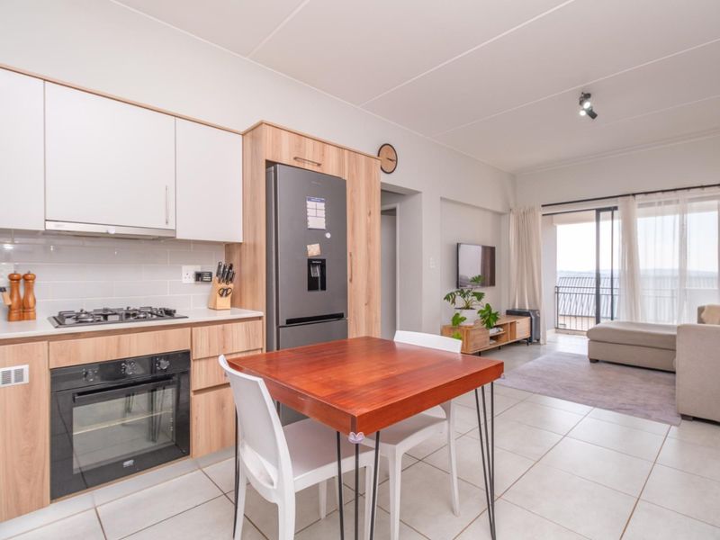 Modern open-plan kitchen and living area featuring light wood cabinetry, gas hob, built-in oven, and direct access to a balcony through sliding doors.