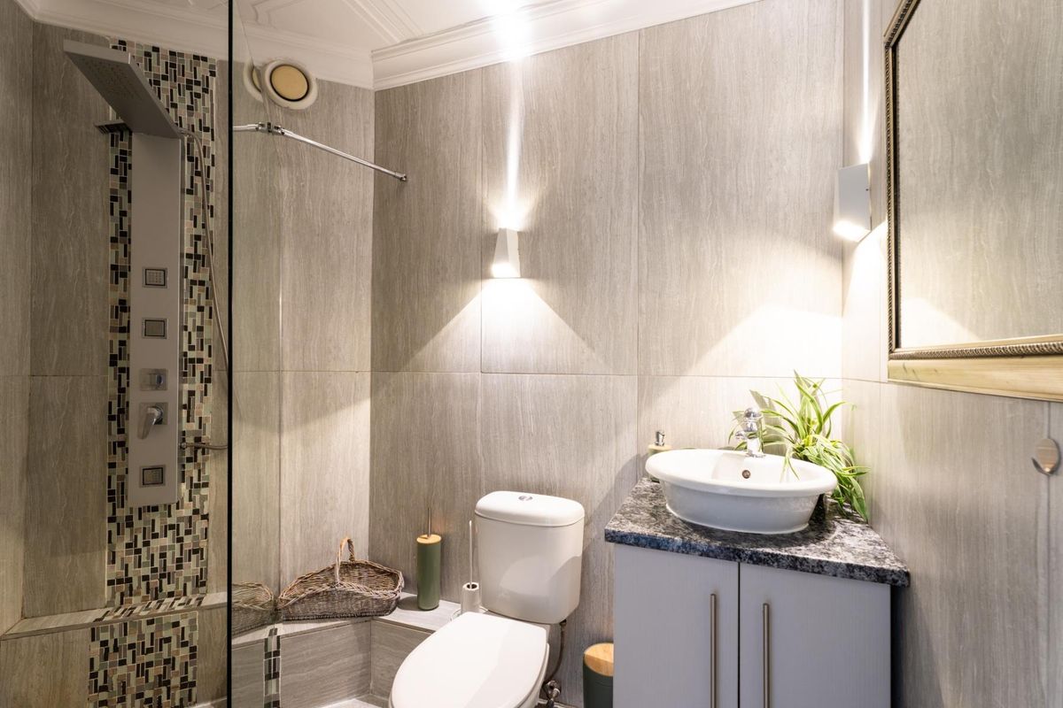 Modern bathroom featuring a glass-enclosed shower with a multi-jet panel, granite-topped vanity with a vessel sink, and contemporary wall lighting.