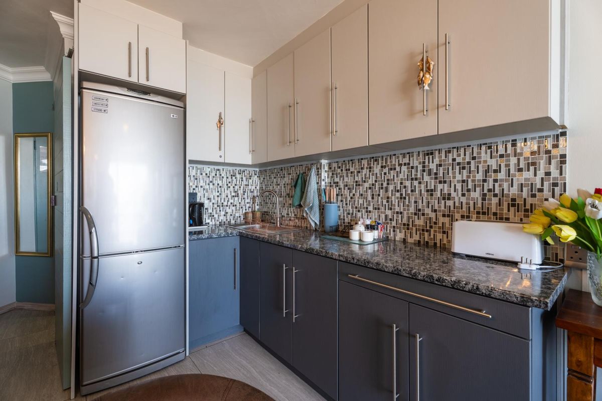A compact, modern kitchen featuring two-tone cabinetry, granite countertops, and a decorative mosaic tile backsplash.