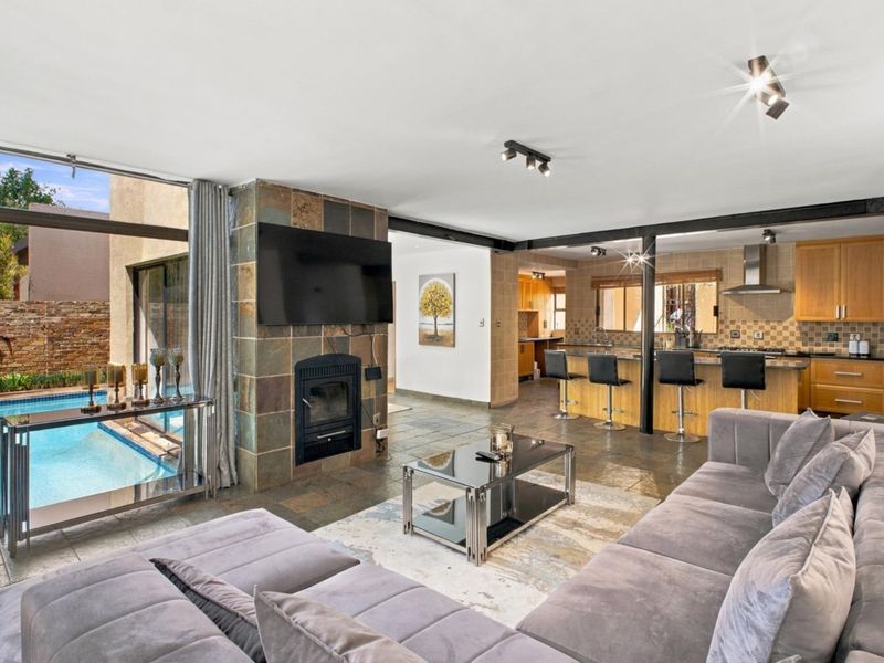 Spacious open-plan living area featuring slate flooring, a stone-clad fireplace, and a modern kitchen with granite countertops, seamlessly connecting to the pool area.