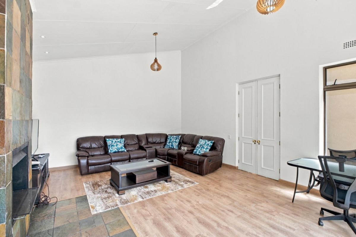 Spacious living room featuring high vaulted ceilings, laminate flooring, and a striking stone-clad fireplace, creating a bright and inviting atmosphere.