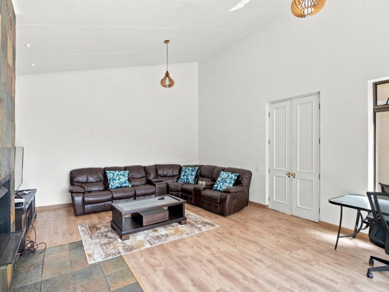 Spacious living room featuring high vaulted ceilings, laminate flooring, and a striking stone-clad fireplace, creating a bright and inviting atmosphere.
