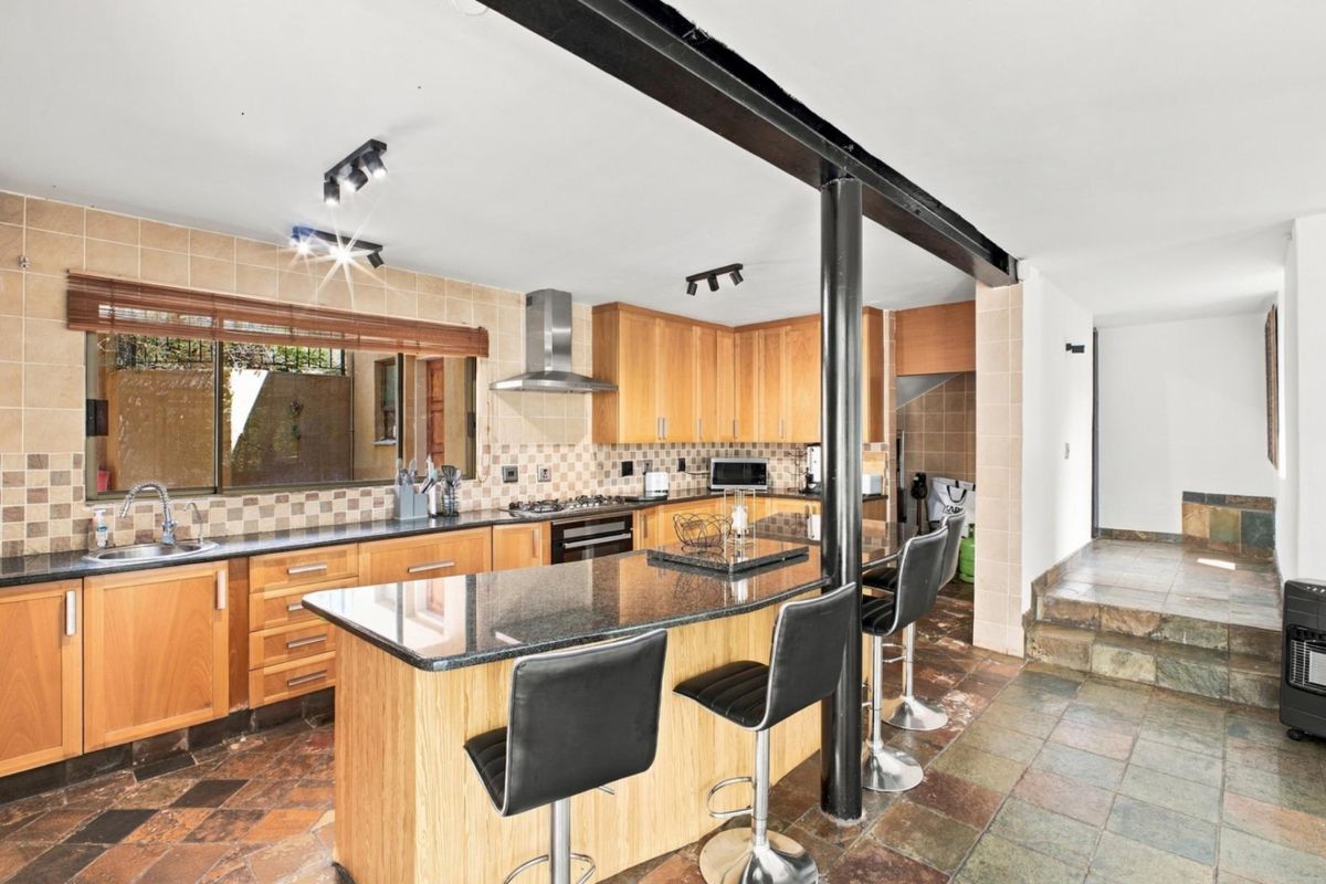 A functional kitchen featuring wooden cabinetry, granite countertops, a gas hob, and a central breakfast bar with a structural support column.