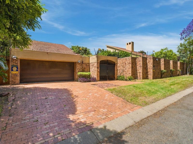Front elevation of a brick-faced house featuring a double garage, paved driveway, and secure boundary wall with electric fencing.