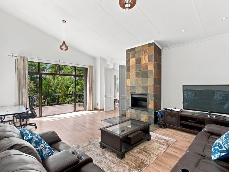 Spacious living room featuring a vaulted ceiling, a prominent stone-clad fireplace, and large sliding glass doors that open onto an outdoor deck area.
