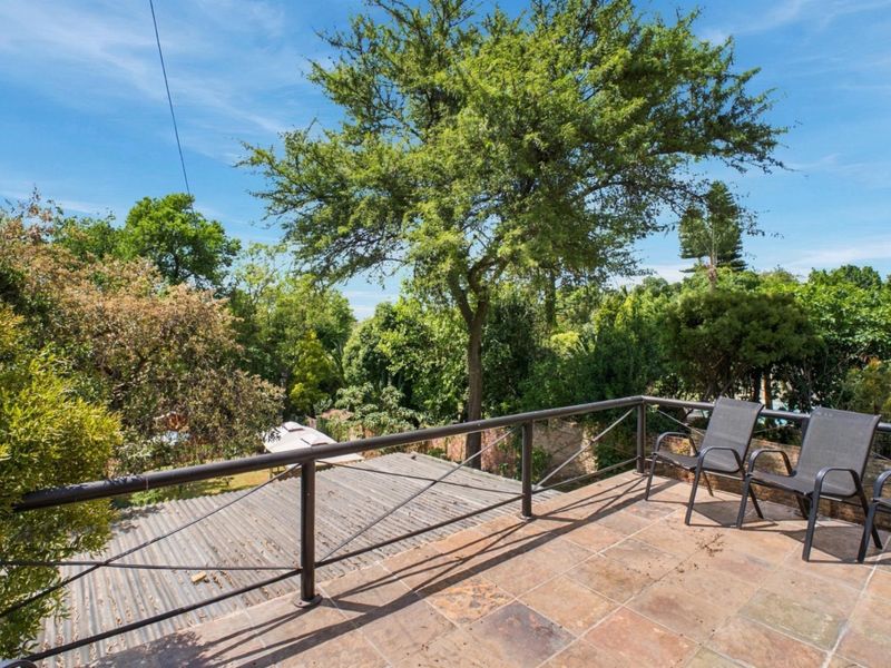 An elevated balcony featuring tiled flooring and a metal railing, offering a scenic view of the surrounding mature trees and garden area.