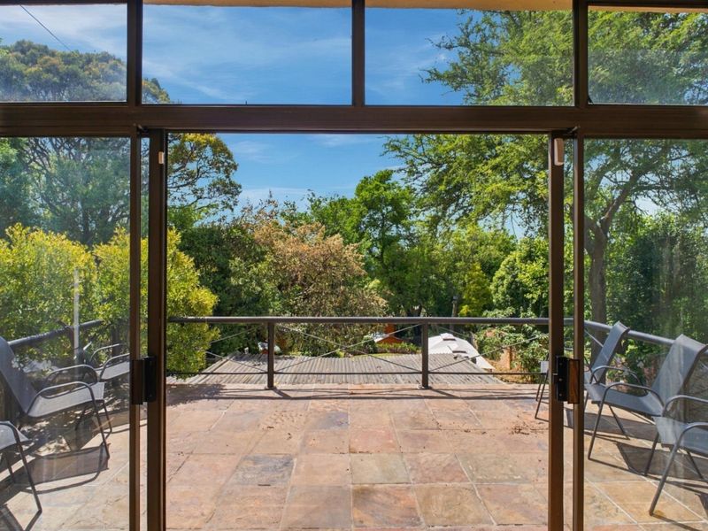 An elevated patio balcony featuring tiled flooring and metal railings, offering a scenic view of the surrounding trees and garden area.