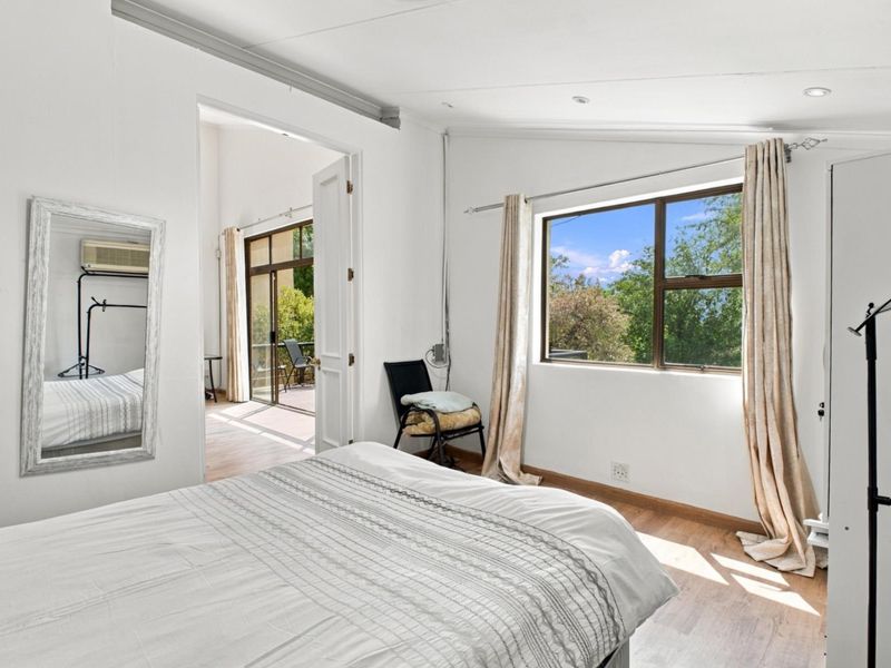 A bright bedroom featuring laminate flooring, recessed lighting, and double doors leading to an adjoining patio area with garden views.