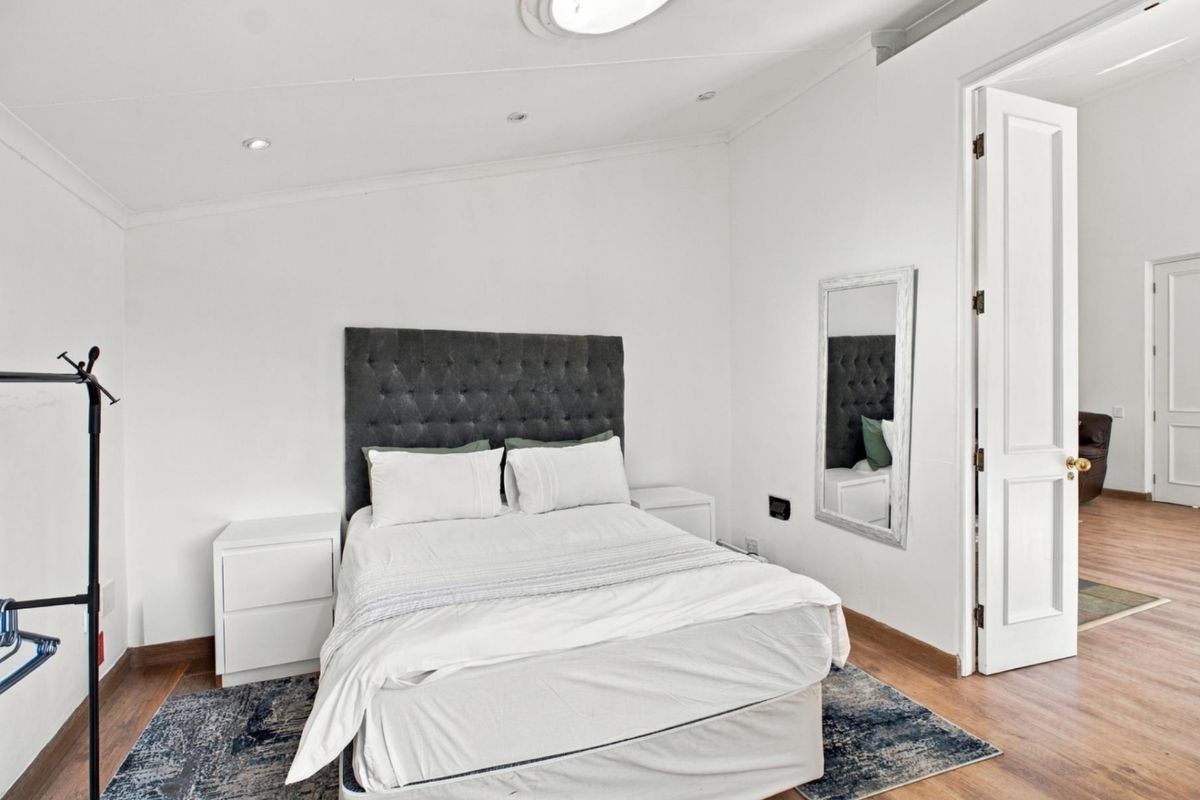 A bright and well-maintained bedroom featuring laminate flooring, recessed downlighting, and a classic panelled door leading to the hallway.