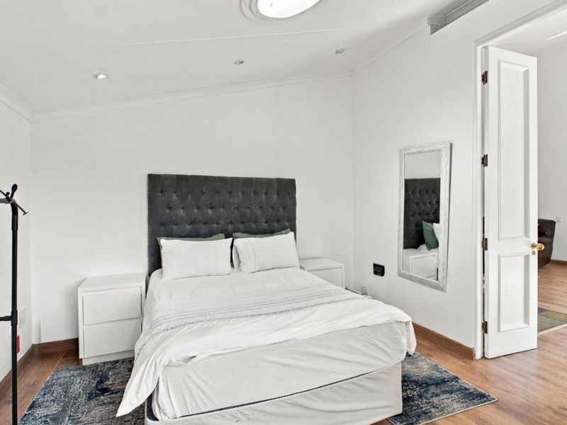 A bright and well-maintained bedroom featuring laminate flooring, recessed downlighting, and a classic panelled door leading to the hallway.