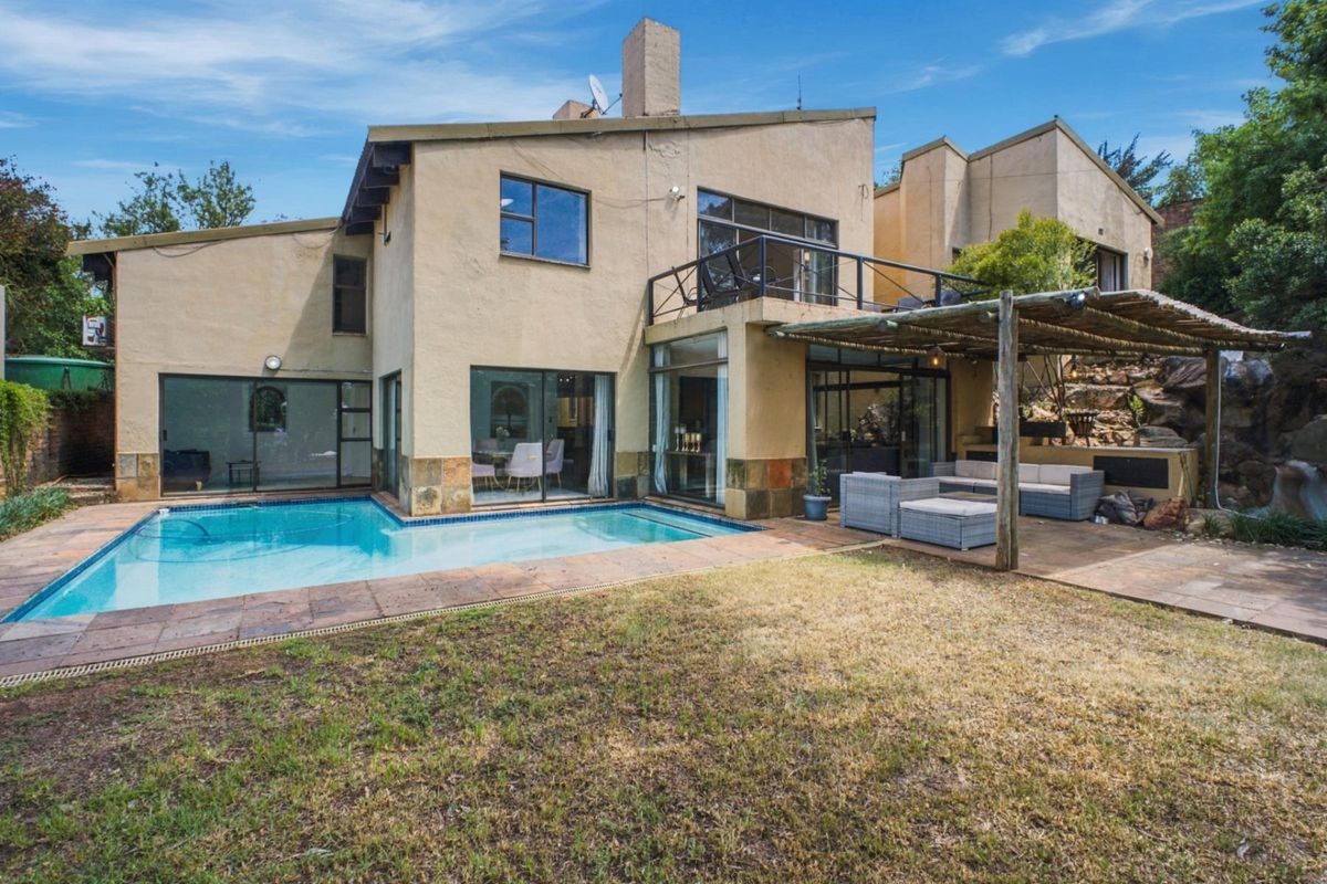 Rear exterior view featuring a swimming pool, covered patio area, balcony, and multi-level architectural design with stone accents.