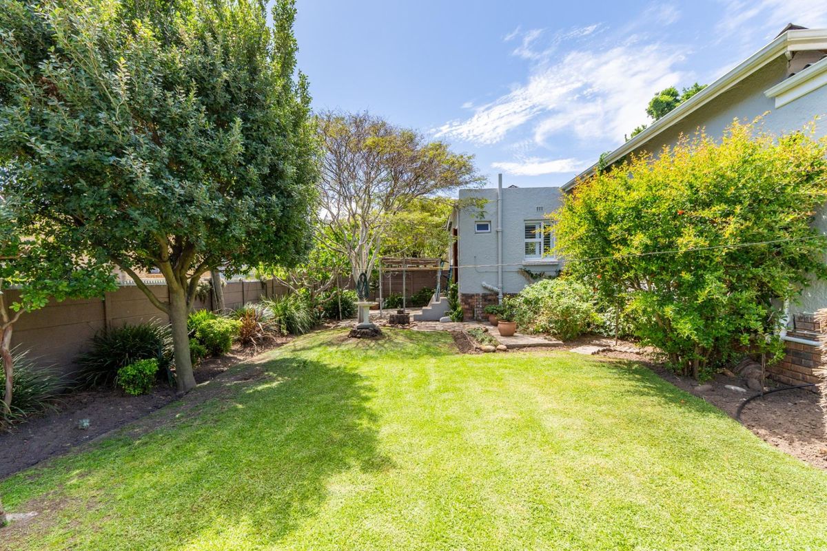 A well-maintained rear garden featuring a lush lawn, mature trees, and a paved area adjacent to the property's exterior wall.