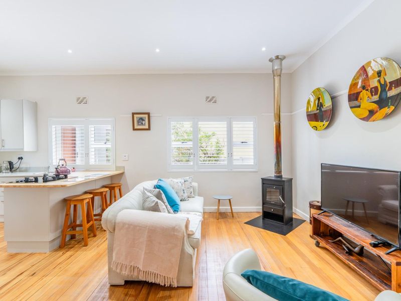 Open-plan living area featuring hardwood flooring, a modern freestanding fireplace, and a functional kitchen with a breakfast island and shutter blinds.