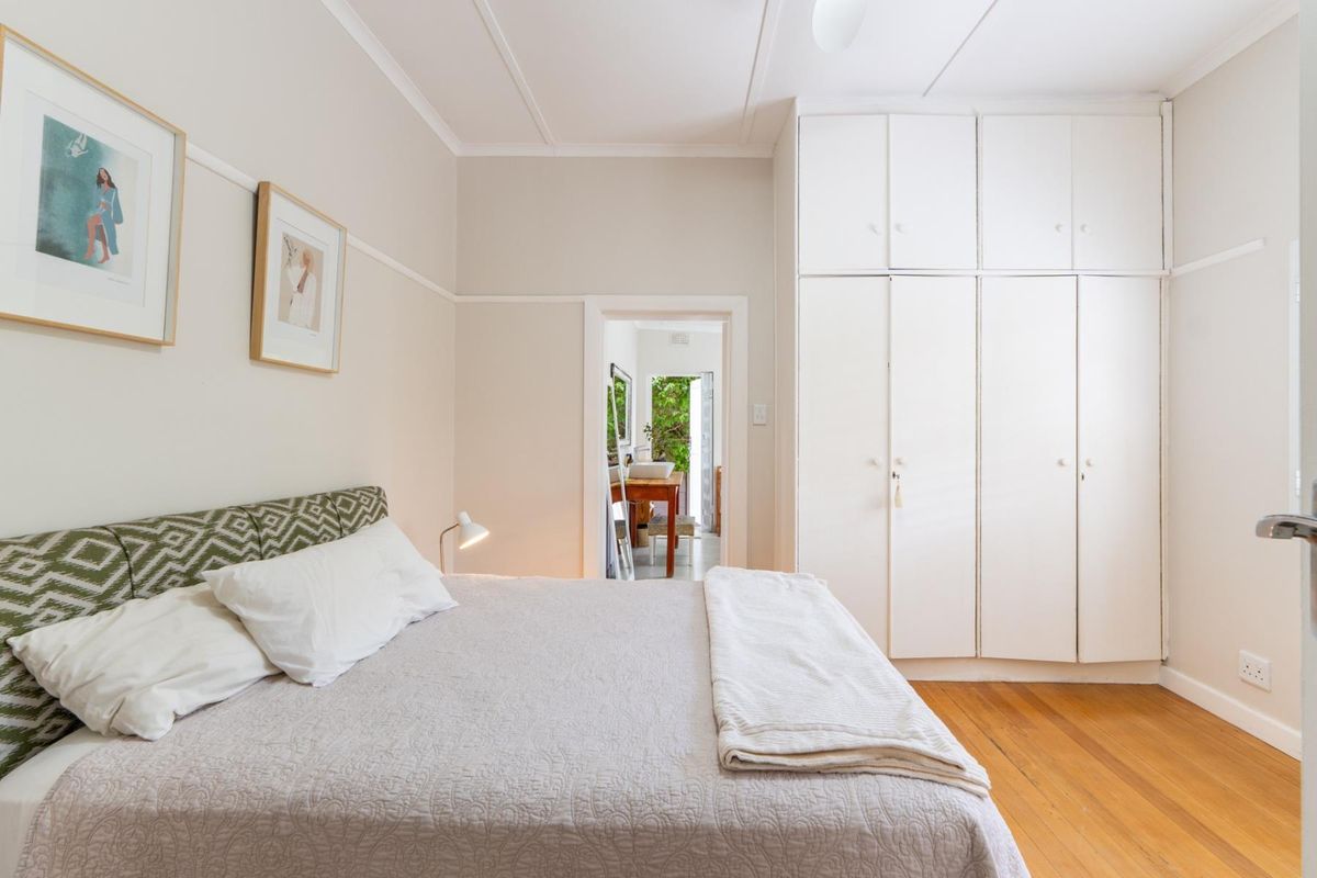 A well-maintained bedroom featuring classic hardwood flooring, built-in floor-to-ceiling cupboards, and traditional architectural details like picture rails.