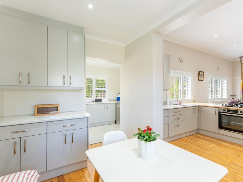 A bright and modern kitchen featuring light grey cabinetry, integrated oven with gas hob, hardwood flooring, and a functional scullery area.