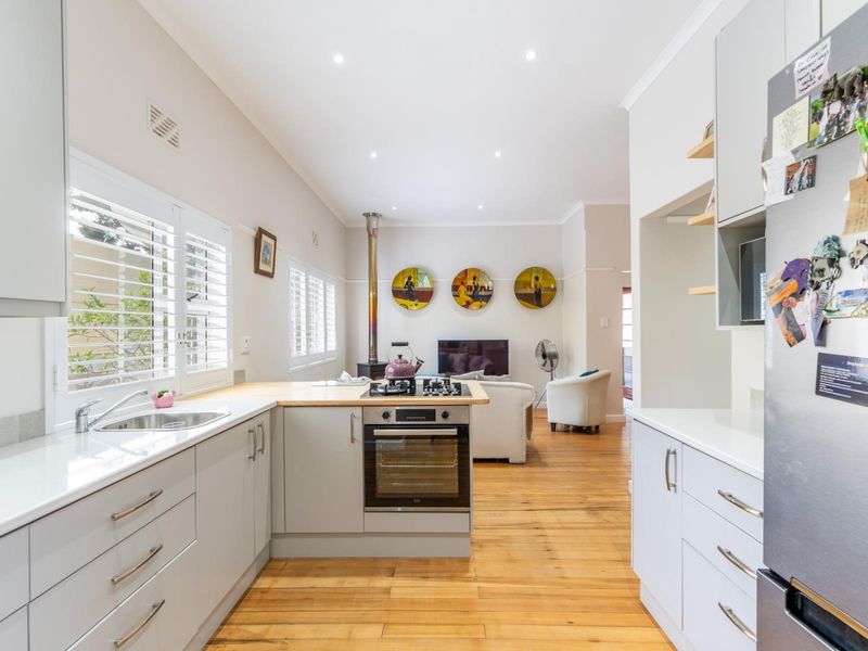 Bright open-plan kitchen and living area featuring modern cabinetry, timber flooring, a gas hob, and a cozy wood-burning fireplace.