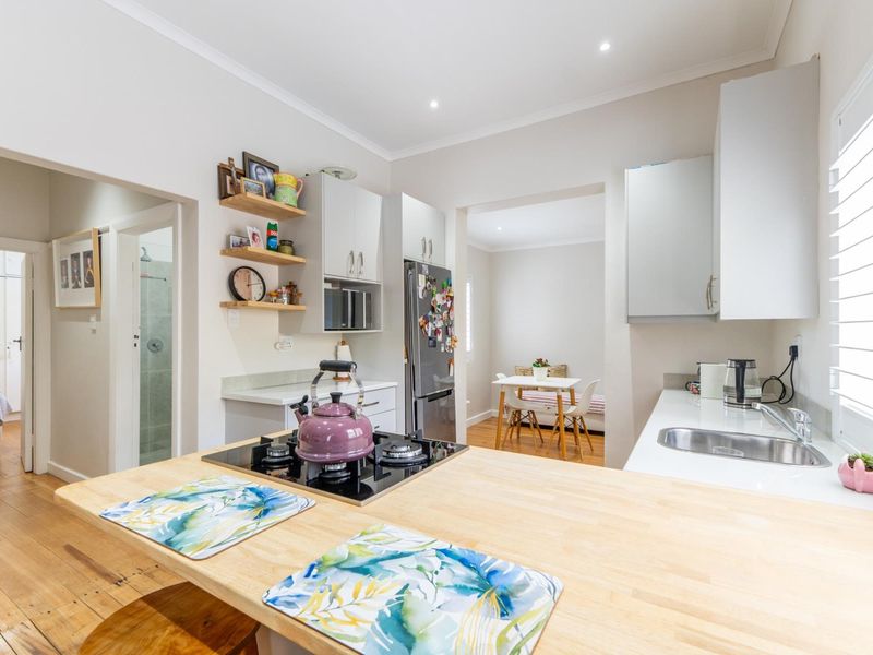 Modern kitchen featuring timber countertops, gas hob, built-in cabinetry, and stainless steel sink, with an open-plan layout leading to an adjacent dining area.