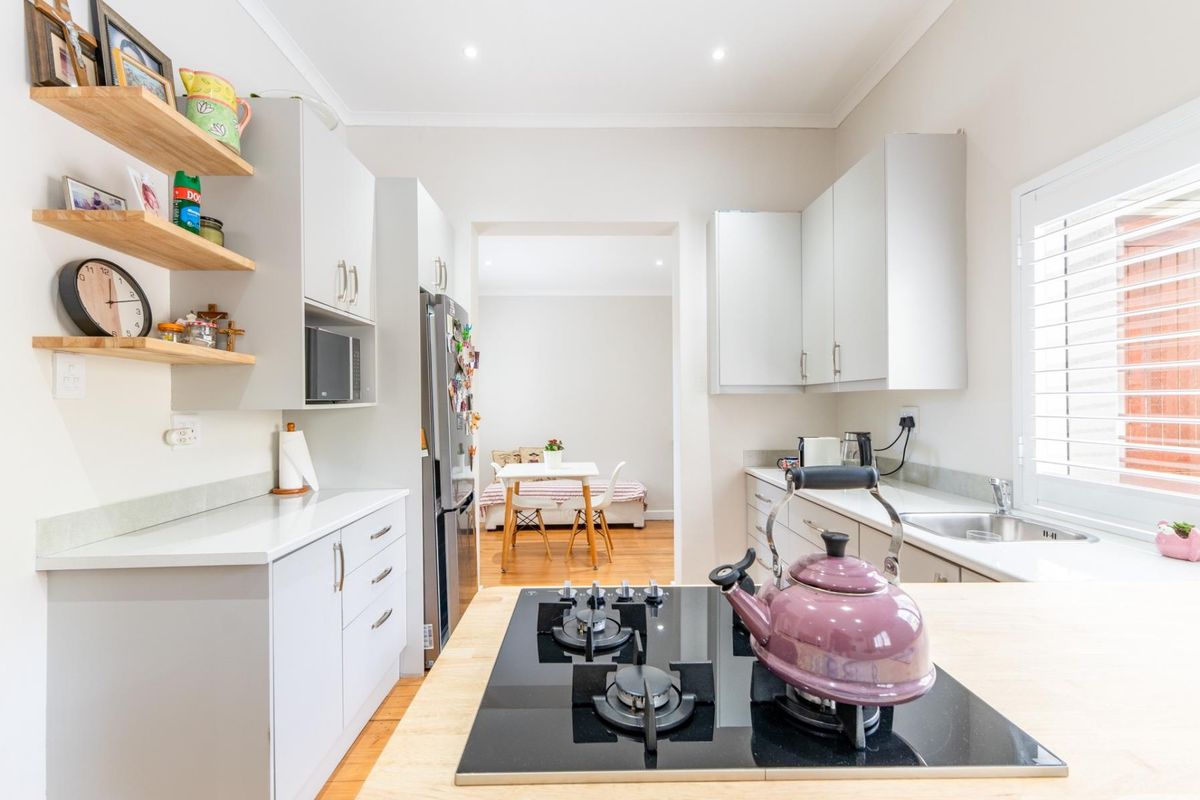 Modern kitchen featuring light grey cabinetry, stone countertops, a gas cooktop, and floating timber shelving, with an adjacent dining area visible.