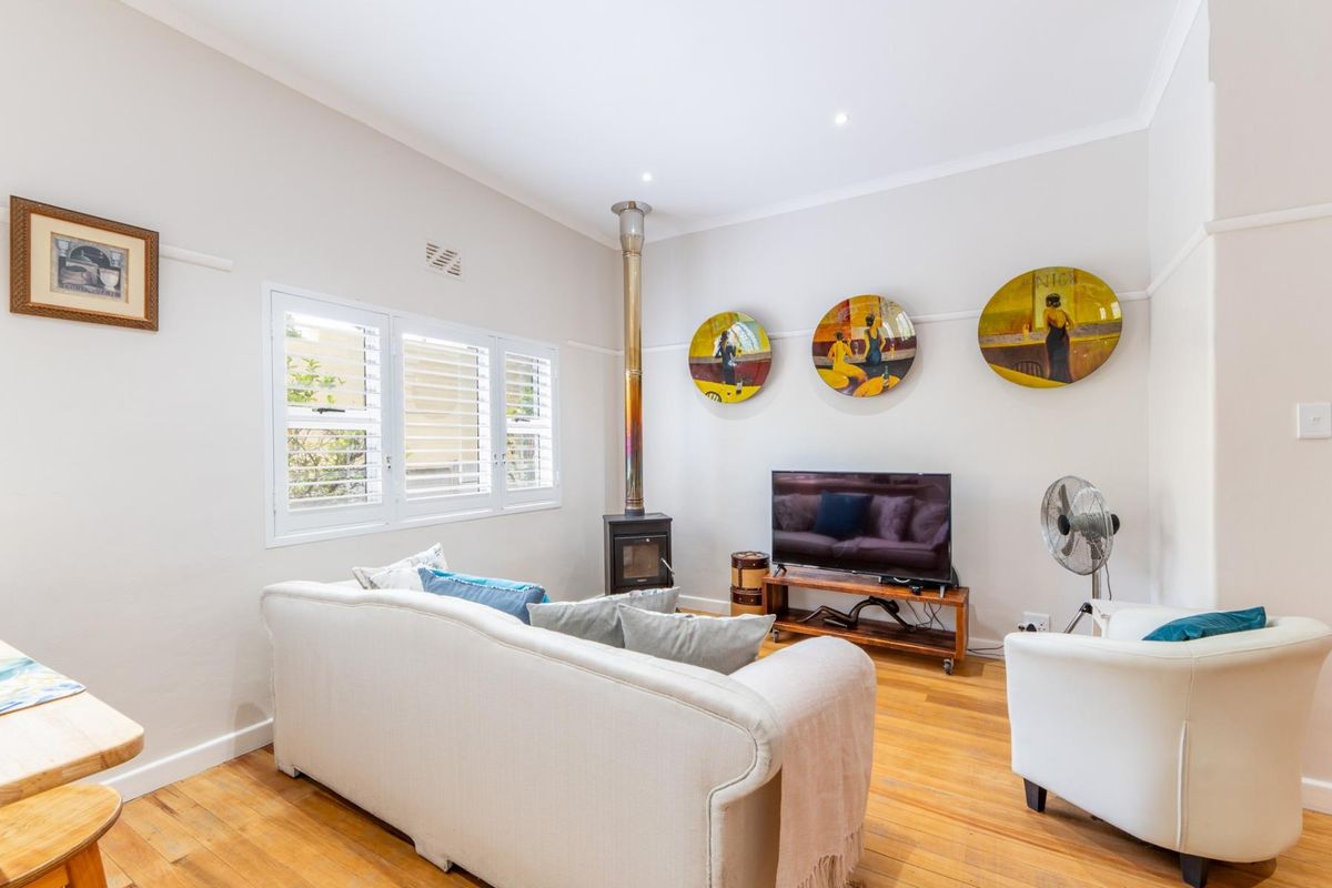 A bright living room featuring polished hardwood flooring, a wood-burning fireplace, and plantation shutters, creating a warm and inviting atmosphere.