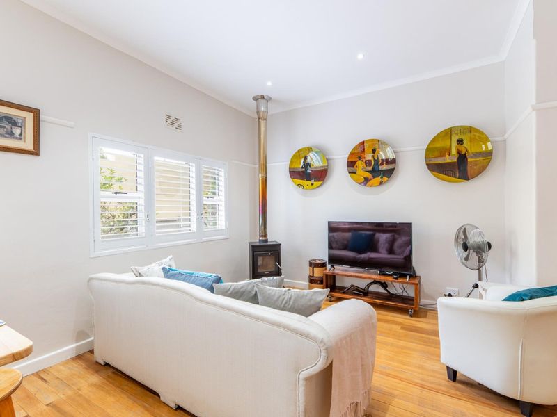 A bright living room featuring polished hardwood flooring, a wood-burning fireplace, and plantation shutters, creating a warm and inviting atmosphere.