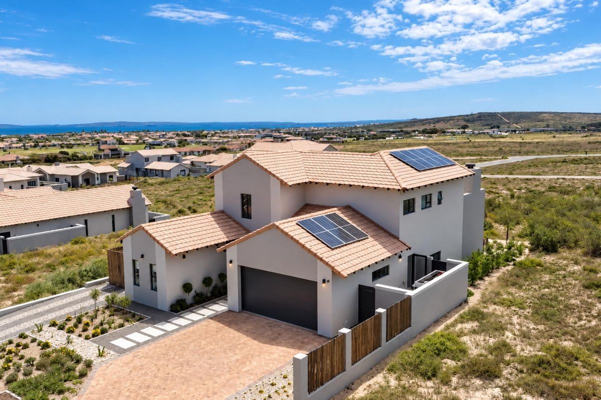 Aerial view of a modern two-story residence featuring a tiled roof, integrated solar panels, a paved driveway, and a secure boundary wall.