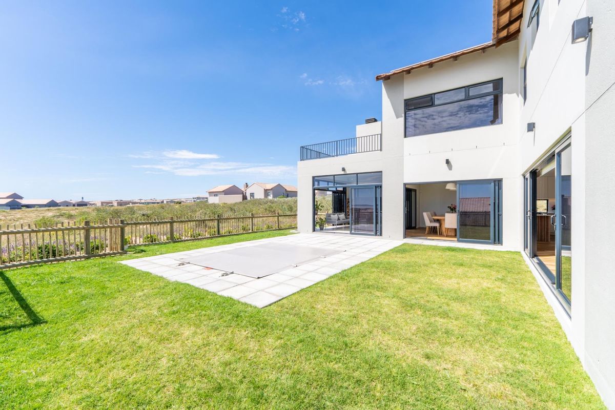 Rear view of a modern two-story home featuring a lawn, paved patio area with a covered swimming pool, and large sliding glass doors.