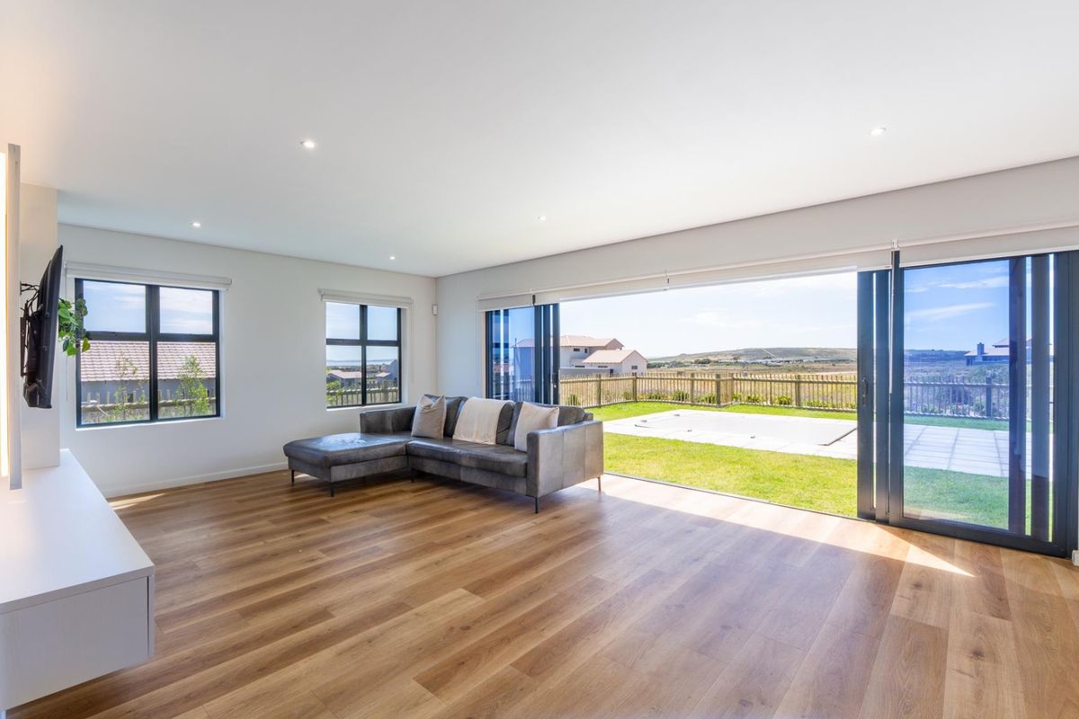 Spacious living room featuring modern laminate flooring, recessed lighting, and large aluminium stacking doors that open onto a private garden and patio area.