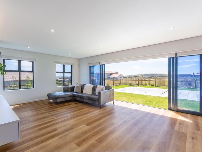Spacious living room featuring modern laminate flooring, recessed lighting, and large aluminium stacking doors that open onto a private garden and patio area.