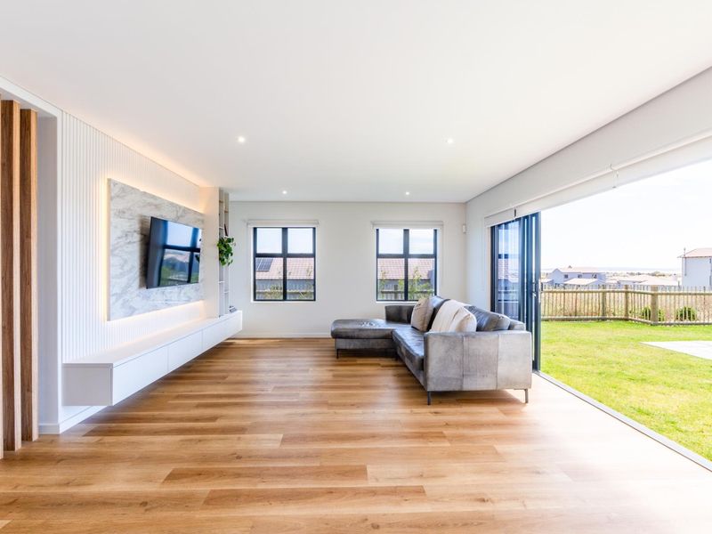 Modern living room featuring timber flooring, a custom built-in media console with marble feature wall, and large sliding doors opening to the garden.