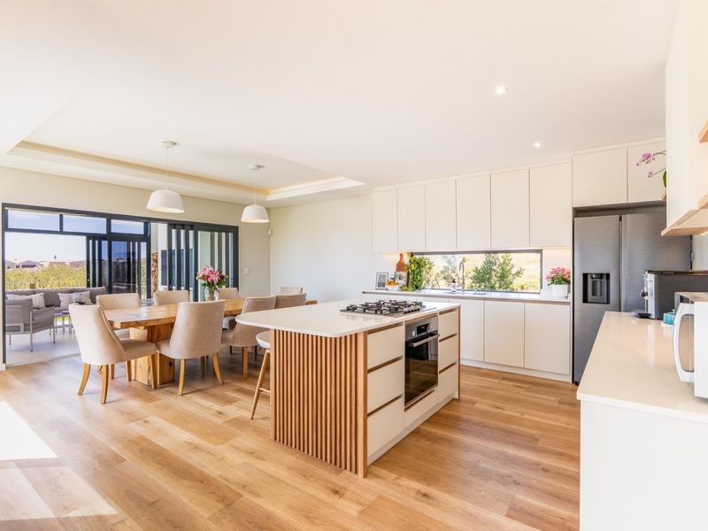 Modern open-plan kitchen and dining area featuring a central island with built-in appliances, sleek cabinetry, and seamless access to an outdoor patio.
