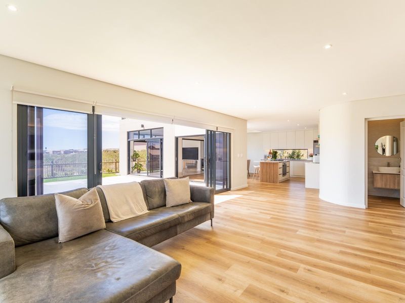 Spacious open-plan living area featuring modern kitchen, light wood flooring, and large sliding doors opening to an outdoor patio.