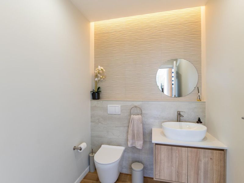 Modern guest bathroom featuring a wall-hung toilet, wood-finish vanity with vessel sink, and a stylish textured feature wall with integrated accent lighting.