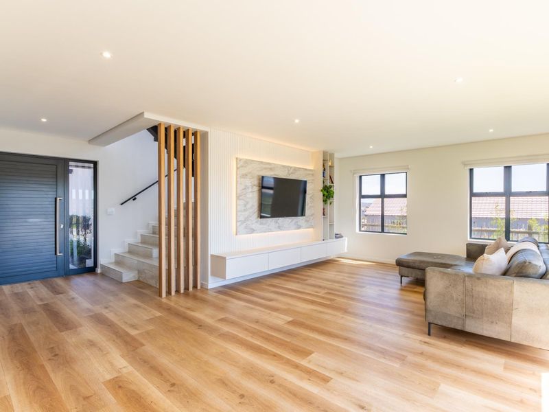 Modern open-plan living area featuring timber flooring, a stone-clad media wall with built-in cabinetry, and a stylish timber slat staircase partition.
