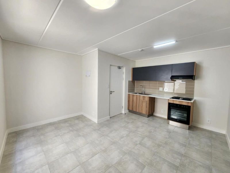 A clean, modern open-plan living and kitchen area featuring tiled floors, contemporary cabinetry, and integrated cooking appliances in a well-maintained space.