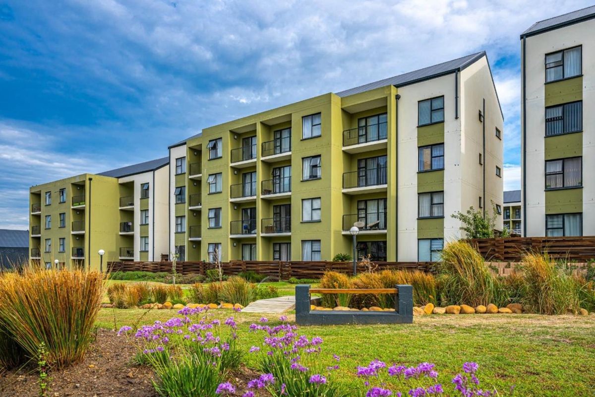 A view of the rear apartment building facade featuring multiple balconies, modern architectural design, and well-maintained landscaped garden areas.